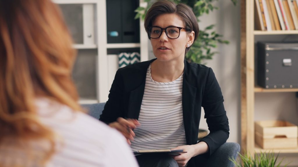 a-woman-sitting-on-a-couch-talking-to-another-woman-rqr2pntpmha