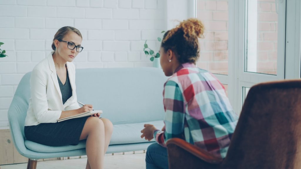 Professional psychologist is listening to troubled African American girl patient and writing in notebook while her client is speaking. Profession, mental health and people concept.